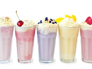 Five colorful fruit milkshakes topped with whipped cream and fruit.
