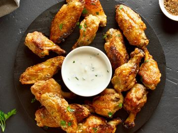 Golden crispy chicken wings with a creamy dipping sauce on a black plate.