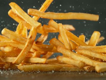 Golden French fries sprinkled with salt in mid-air.