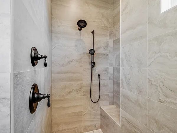 Modern shower with bronze fixtures and beige stone tiles.