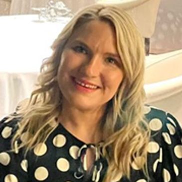 Smiling woman with blonde hair in a black polka dot dress.