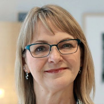 Smiling middle-aged woman with glasses and earrings.