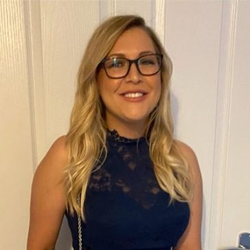 Smiling woman with glasses and long blonde hair in a navy blue dress.
