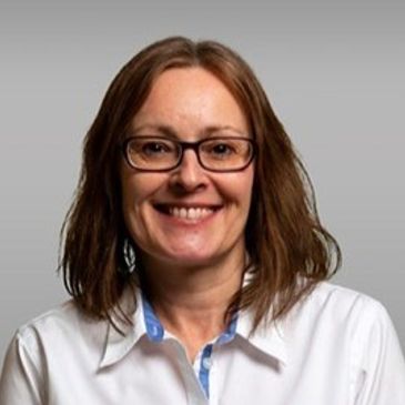 Smiling woman with glasses and brown hair in white shirt.