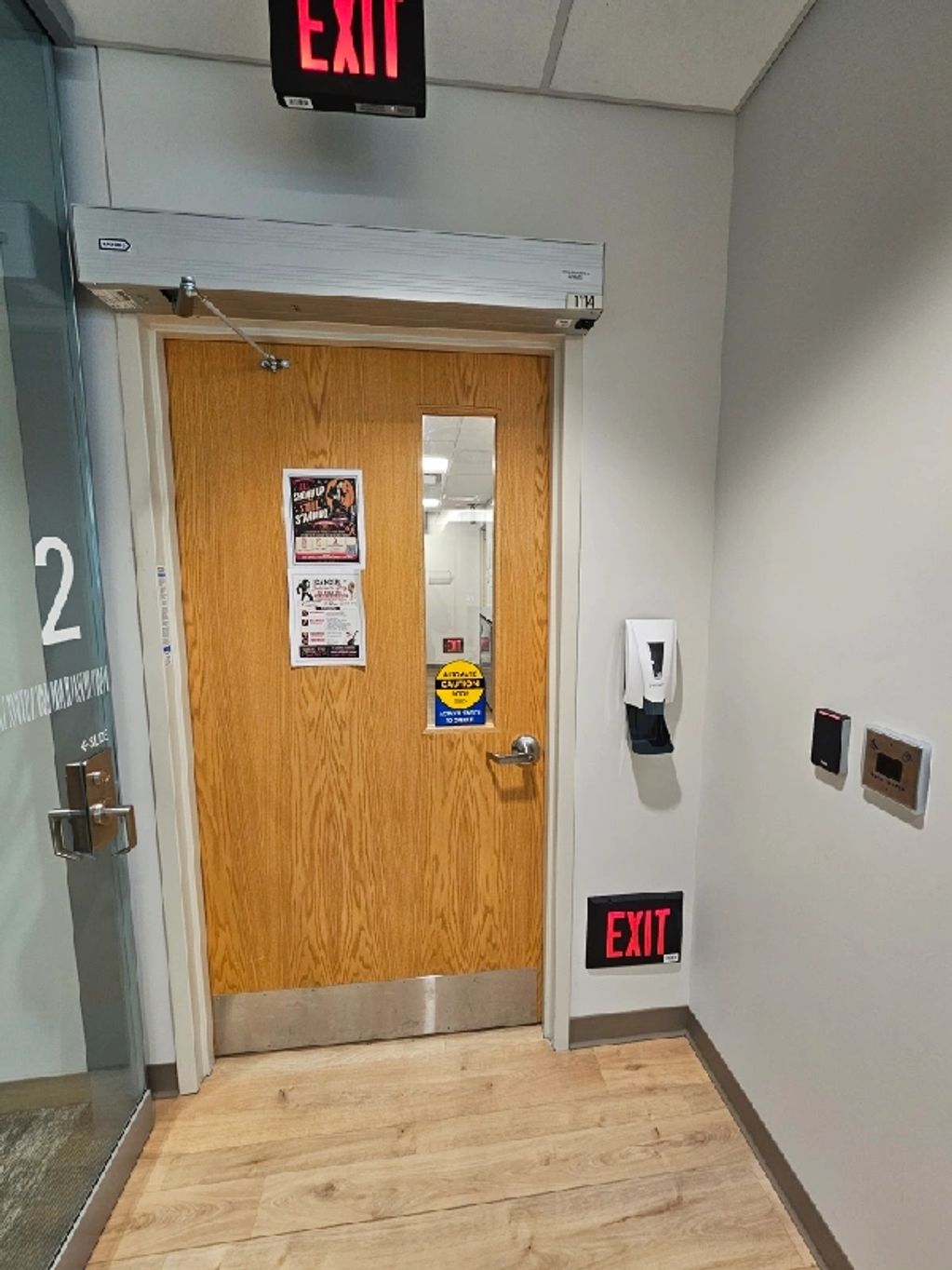 Wooden exit door with exit signs and a hand sanitizer.