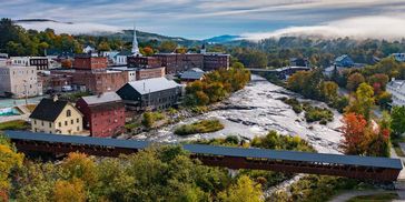 Scenic town with covered bridge over river and autumn foliage.