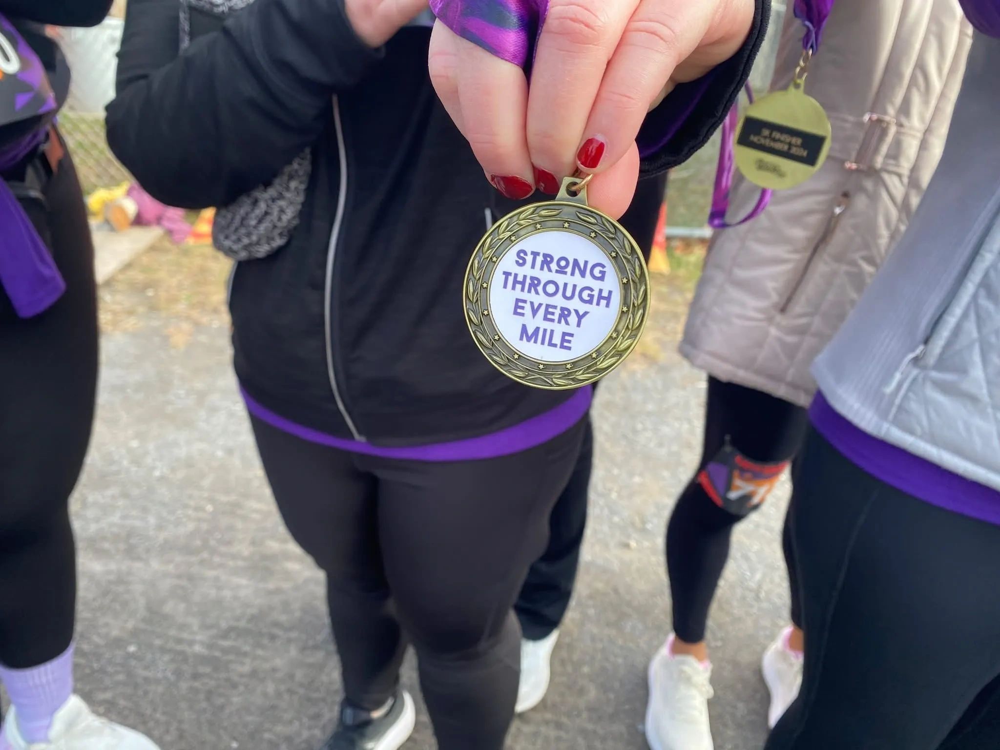 hand holding up a medal that says Strong Through Every Mile in front of someone wearing a black jack