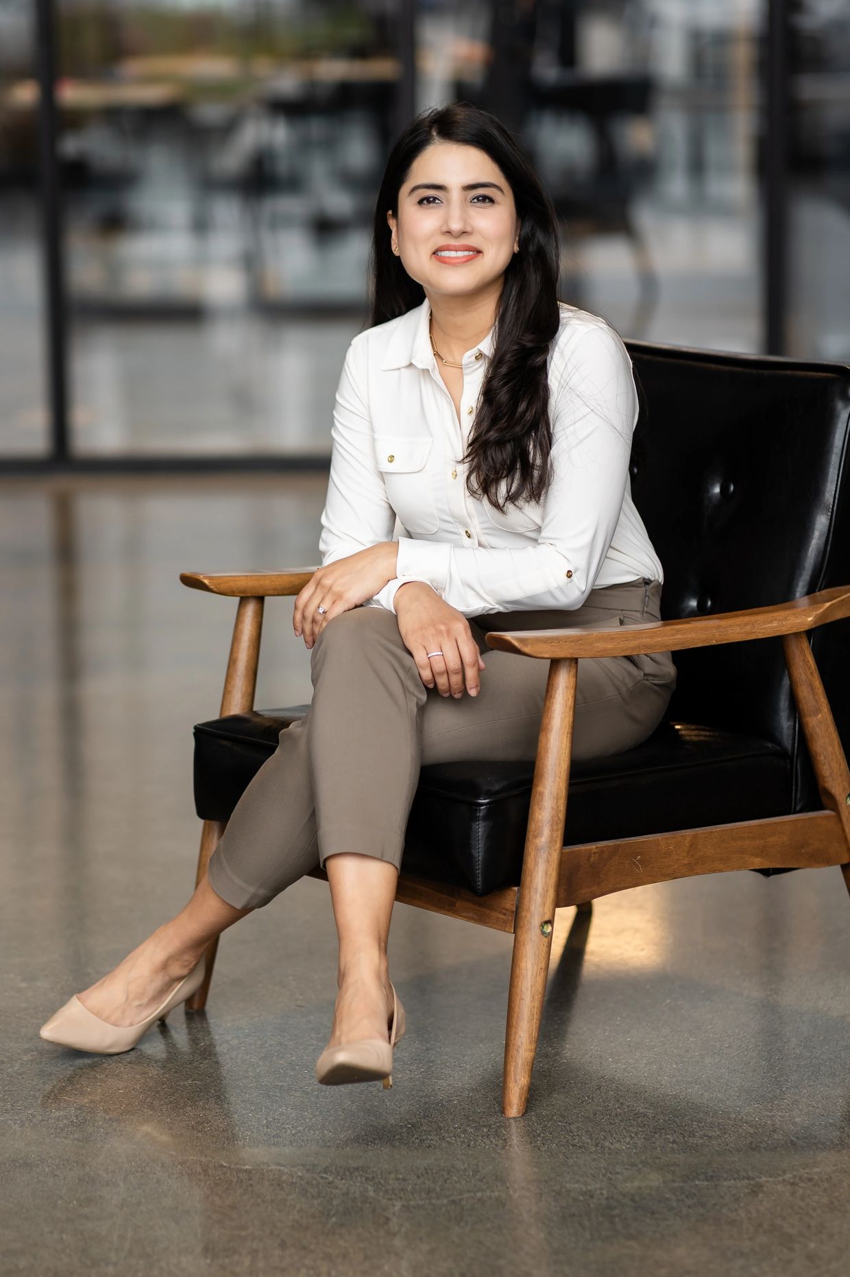 A confident woman in business attire sitting on a modern chair, smiling.