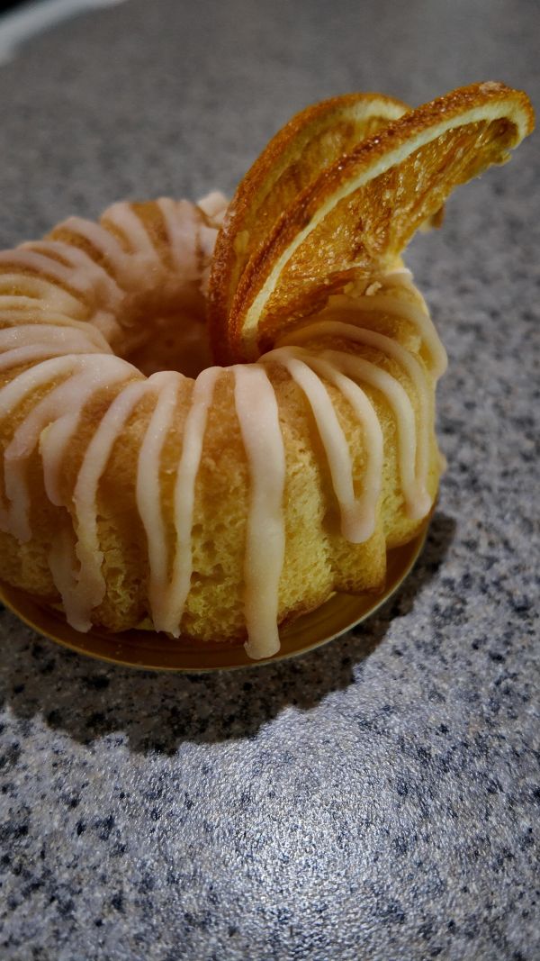 Small bundt cake with icing and dried orange decoration.
