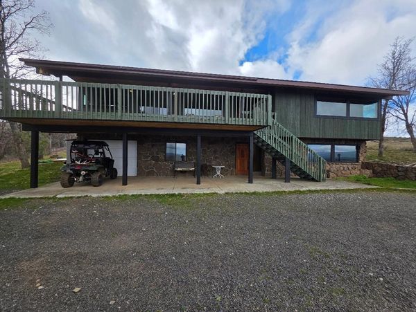 Two-story rustic house with stone and wood exterior, large deck, and ATV parked outside.