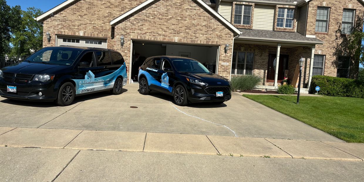 Two branded cleaning service vehicles parked in front of a brick house on a sunny day.