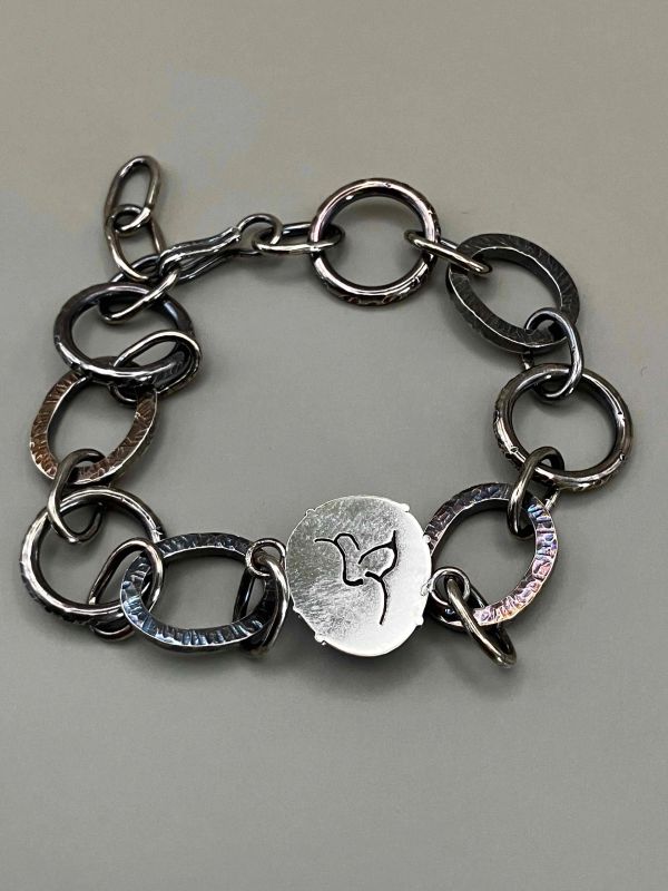 Silver bracelet with large circular links and a hummingbird charm.