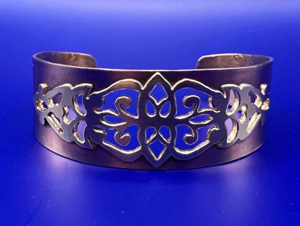 Silver cuff bracelet with intricate cut-out design.