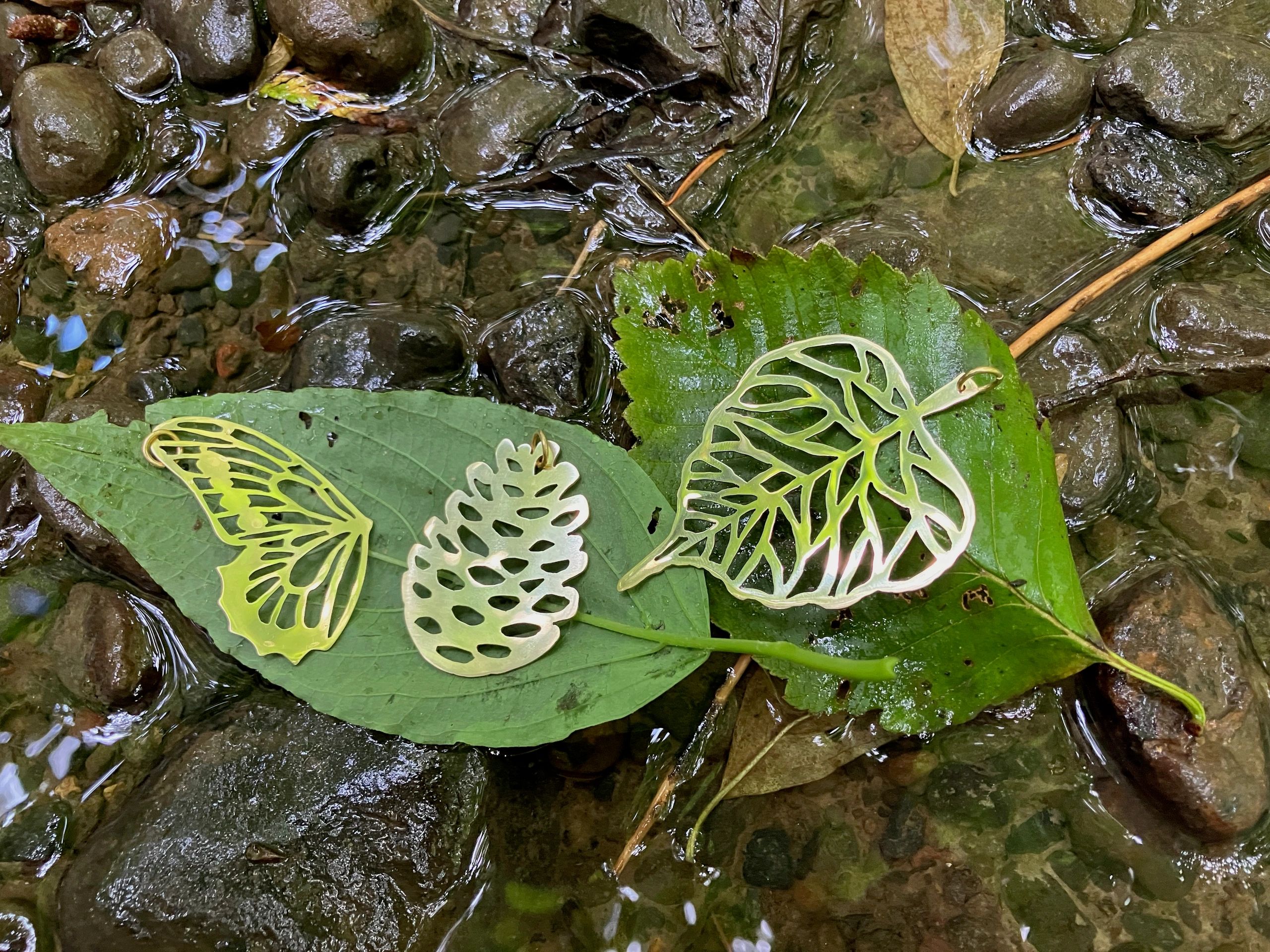 golden images of butterfly, pine cone and leaf sitting on a green leaf in water