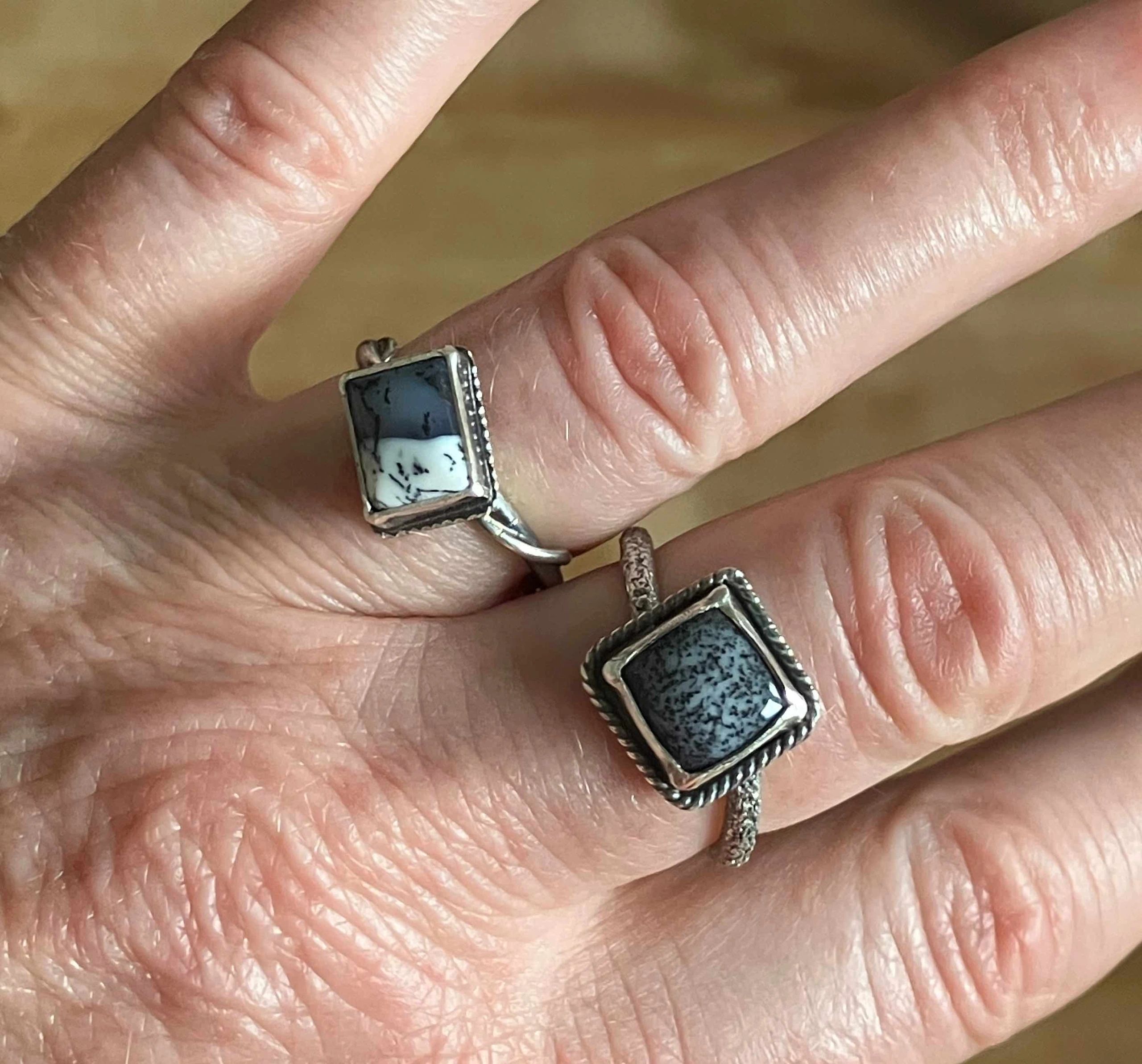 Close-up of hand with silver rings featuring patterned stones.