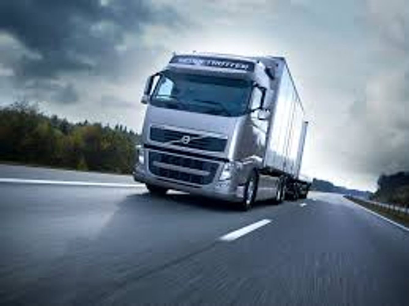 Silver Volvo semi-truck driving on highway under cloudy sky.