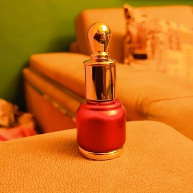 Red nail polish bottle with a golden cap on a beige surface.