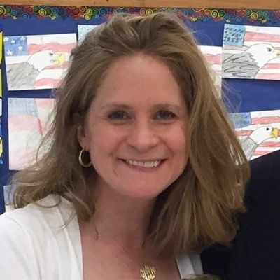 Smiling woman with shoulder-length hair in a classroom setting.