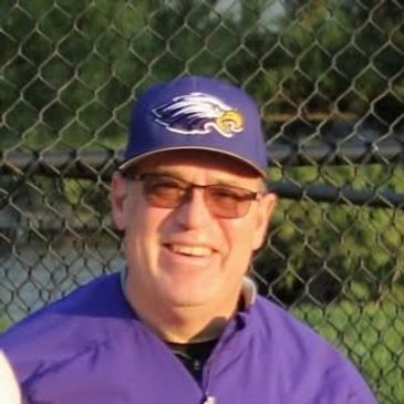 Man smiling wearing a blue sports cap and jacket.
