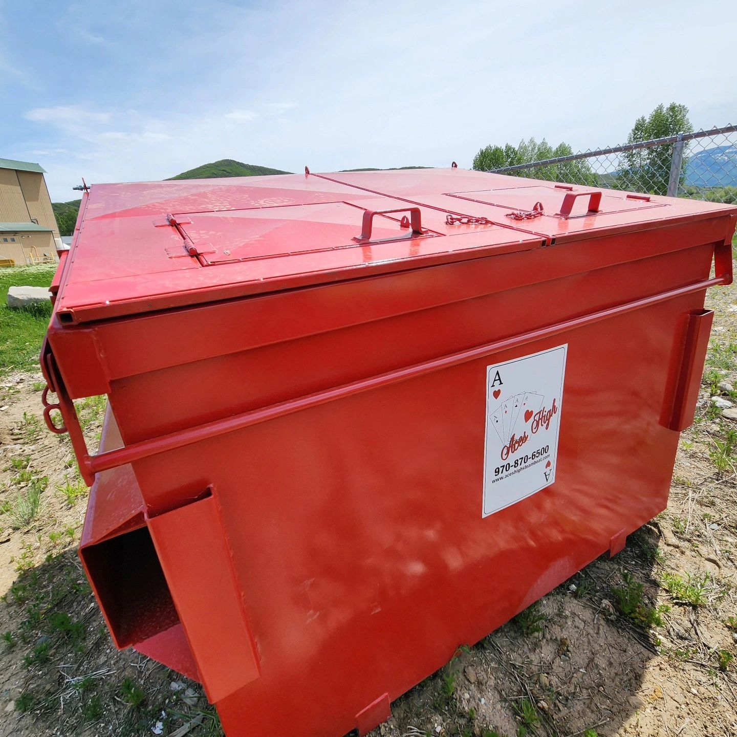 Large red dumpster with a company logo outdoors under a clear sky.
