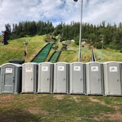 A row of portable toilets lined up outdoors near a grassy hill with ski ramps.