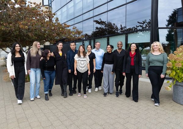 A diverse group of people standing and smiling outside a modern building.