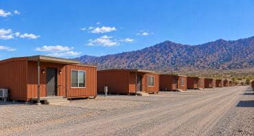 Row of brown cabins with desert mountains in the background.