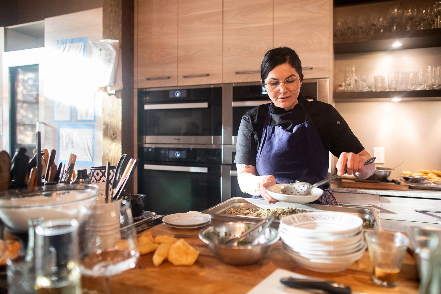 Woman in an apron serving food in a modern kitchen.