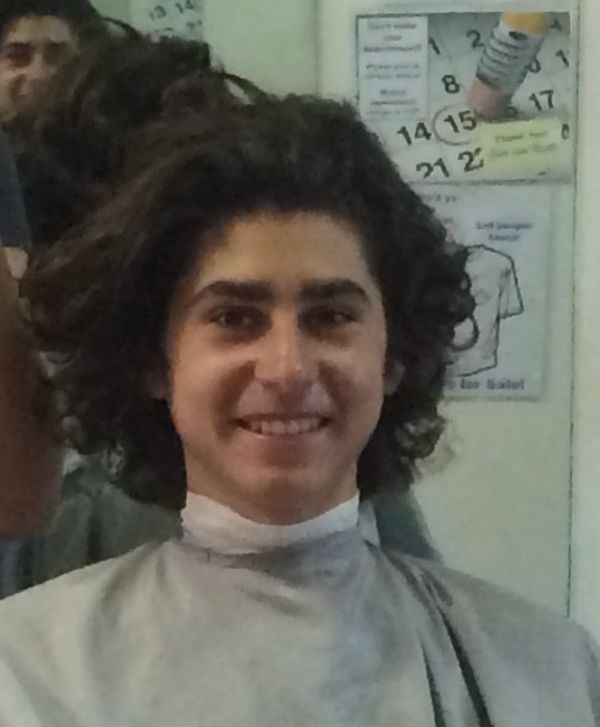 Young man with curly hair smiling at a barbershop.