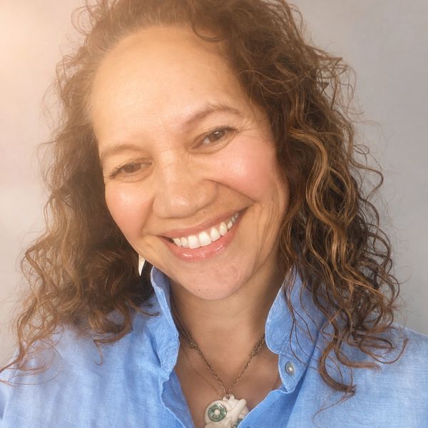 A smiling woman with curly hair wearing a blue shirt and a necklace.