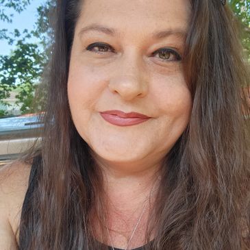 Close-up of a smiling woman with long brown hair and natural makeup outdoors.