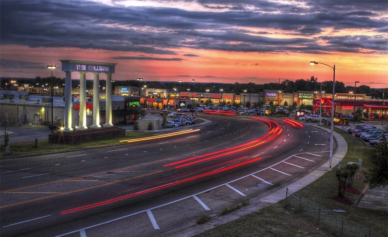 Sunset over a bustling shopping center with light trails on the road.
