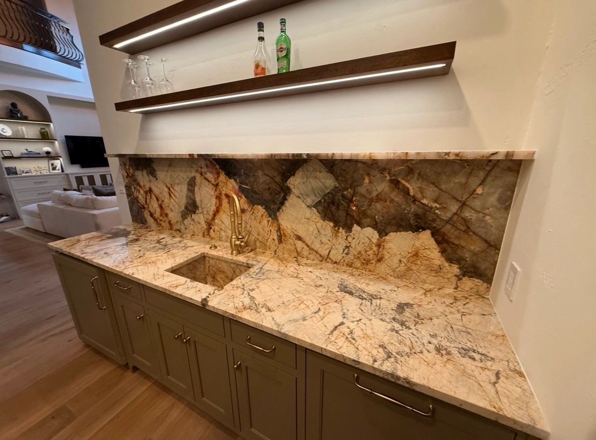 Marble countertop with sink and shelves holding bottles and glasses.