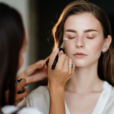 A beautiful young woman with long hair doing makeup for a wedding or photo shoot.