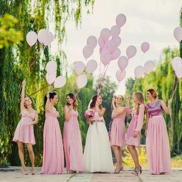 Beautiful smiling bride with bridesmaids walk outdoors holding pink balloons