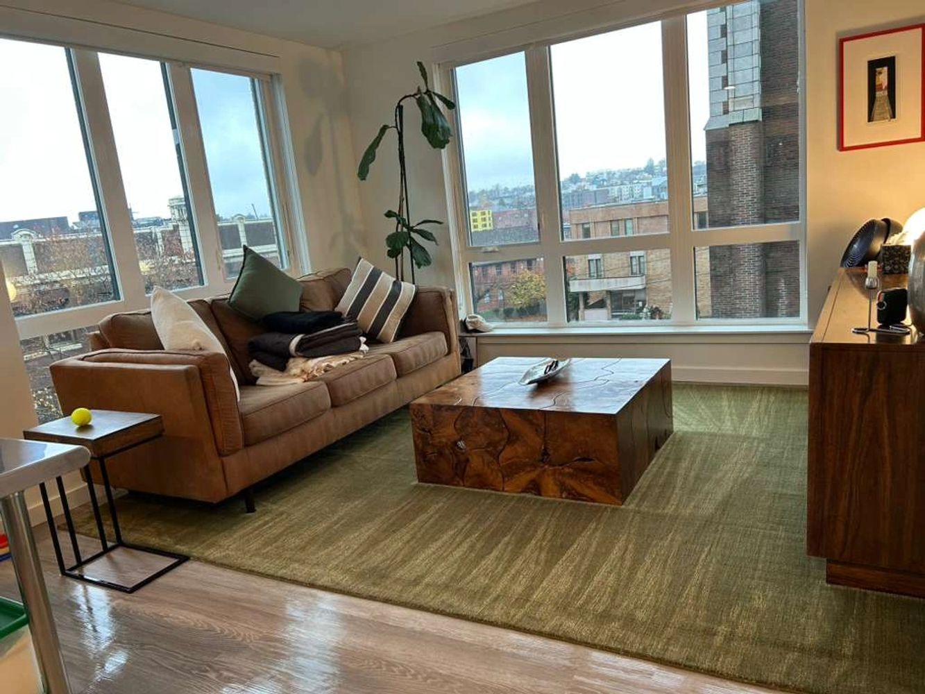 Bright living room with large windows, a brown sofa, and a wooden coffee table.