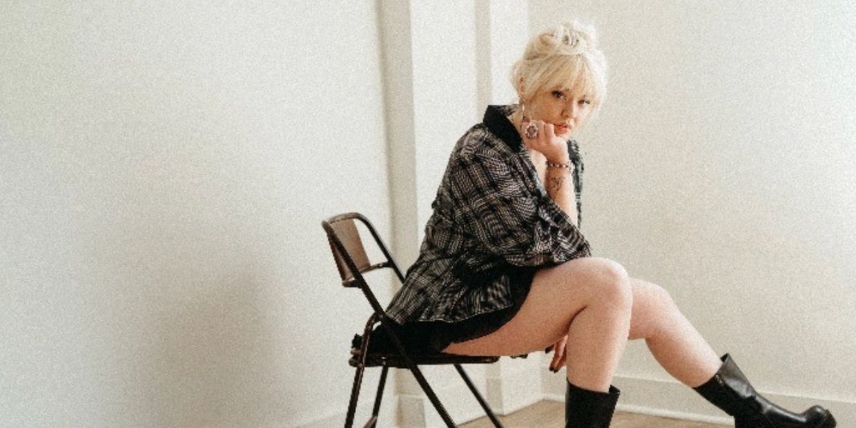 Fashionable woman with blonde hair sitting on a chair in a minimalist room.