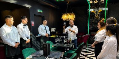 Restaurant staff attentively listen to a man explaining wine.