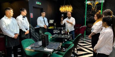 Restaurant staff attentively listen to a man explaining wine.