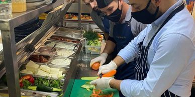 Chefs in masks and gloves preparing vegetables in a professional kitchen.