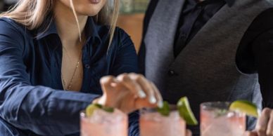 Bartender garnishing cocktails at a bar with a colleague watching.
