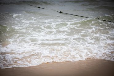 Waves gently washing onto a sandy beach with floating ropes.
