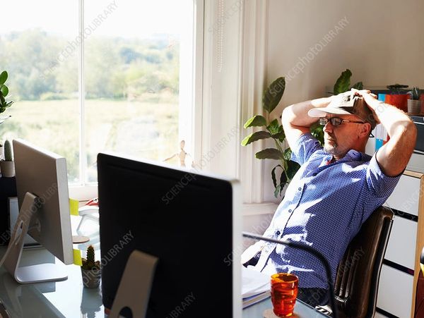 Man in blue shirt stressed at office desk with two computer monitors.