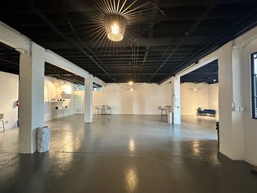 Full view of venue space - concrete flooring, black hanging light fixtures from ceiling, white walls