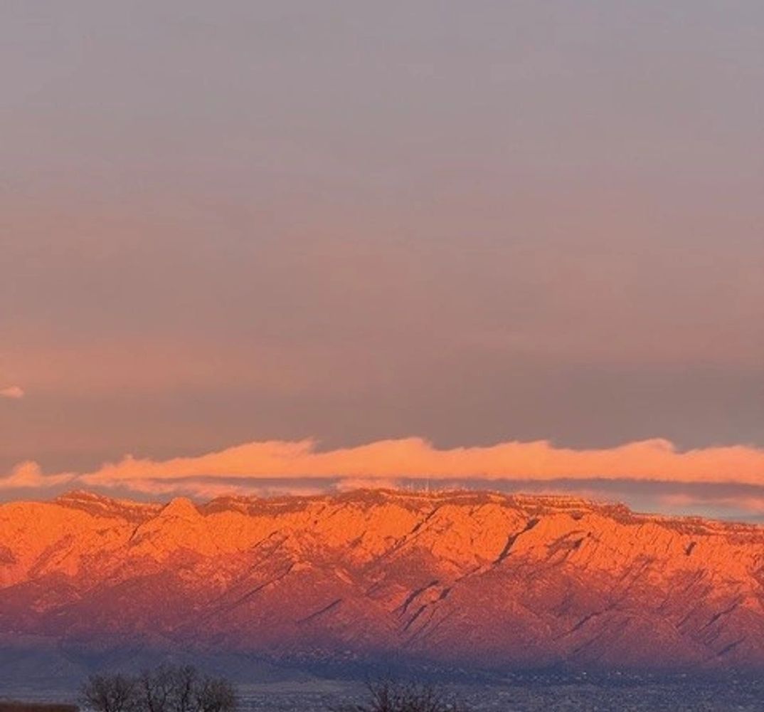 Mountain range bathed in warm sunset light under a soft sky.