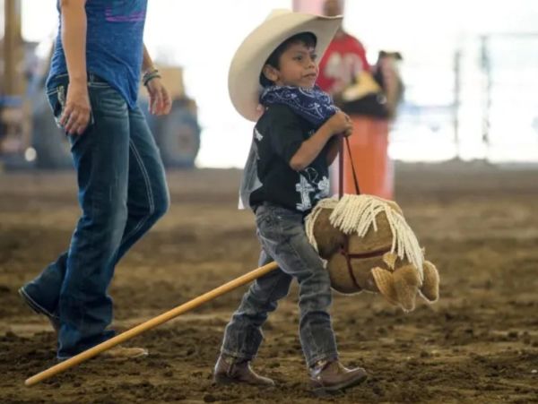Young boy dressed as a cowboy riding a hobby horse indoors.