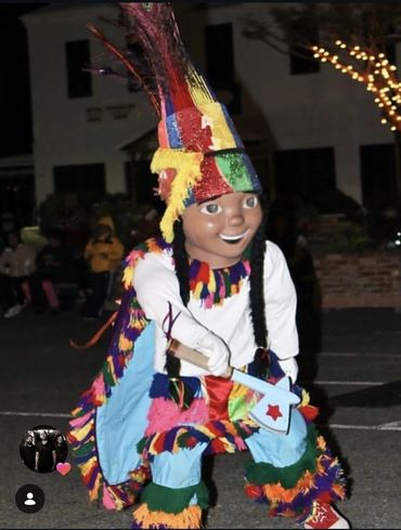 Person in colorful traditional costume with large headpiece and wooden axe.