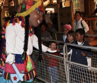 Person in colorful costume interacting with kids behind barriers.