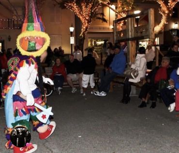 Person in colorful clown costume performing outdoors at night.