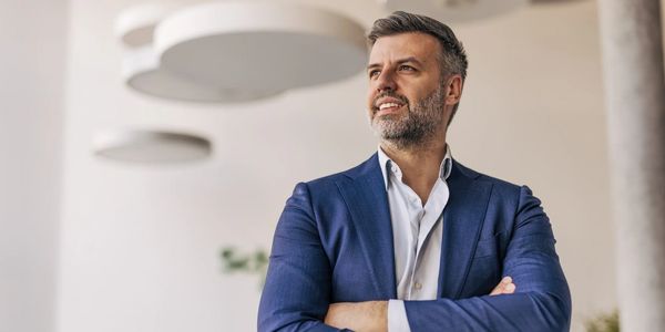 Confident businessman in blue suit standing with arms crossed indoors.